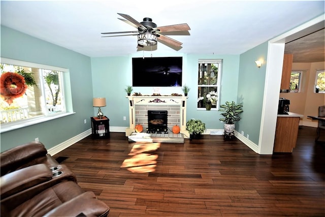 living room featuring ceiling fan, a stone fireplace, baseboards, and wood finished floors