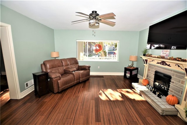 living area featuring a fireplace with raised hearth, wood finished floors, a ceiling fan, visible vents, and baseboards