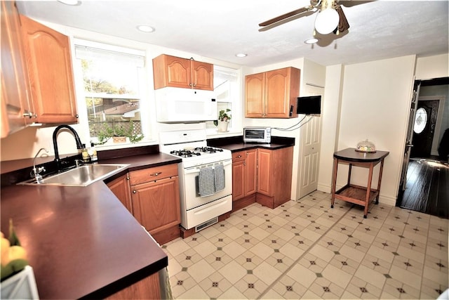 kitchen with white appliances, a ceiling fan, dark countertops, light floors, and a sink
