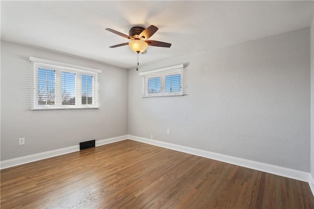 spare room with a ceiling fan, visible vents, baseboards, and wood finished floors