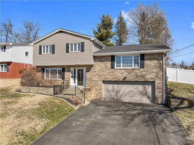 split level home with a garage, brick siding, driveway, and fence