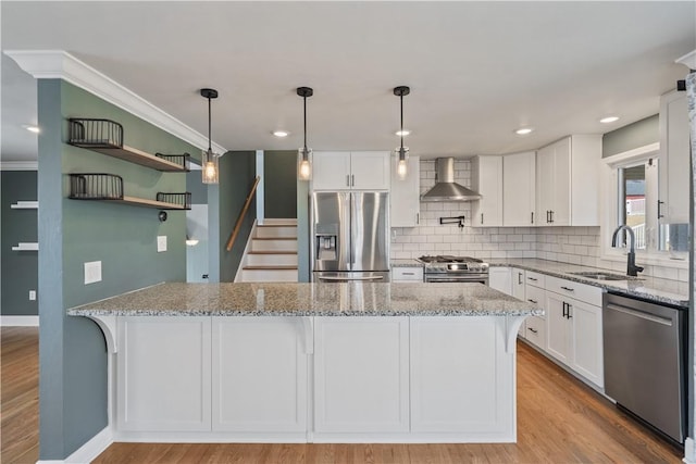 kitchen with light stone counters, stainless steel appliances, wall chimney range hood, white cabinetry, and a sink