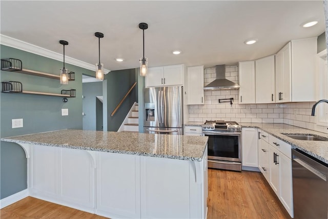 kitchen with light wood finished floors, wall chimney exhaust hood, appliances with stainless steel finishes, light stone countertops, and a sink