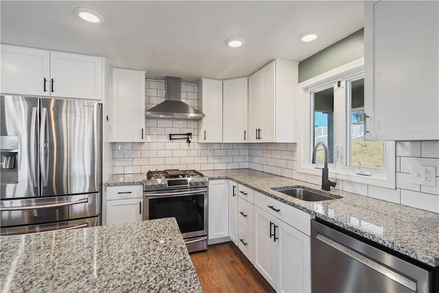 kitchen with dark wood finished floors, stainless steel appliances, white cabinets, a sink, and wall chimney exhaust hood