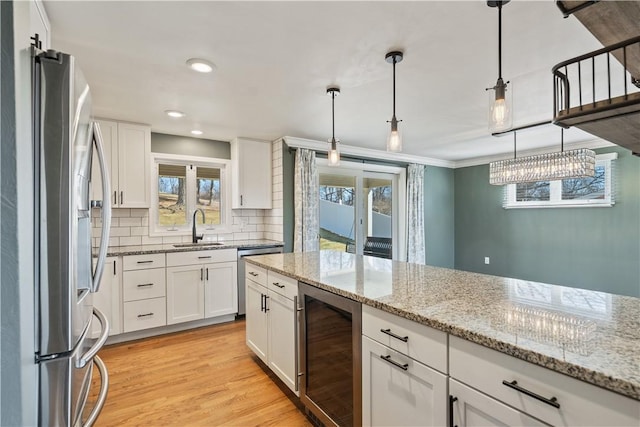 kitchen with light wood finished floors, white cabinets, wine cooler, stainless steel appliances, and a sink