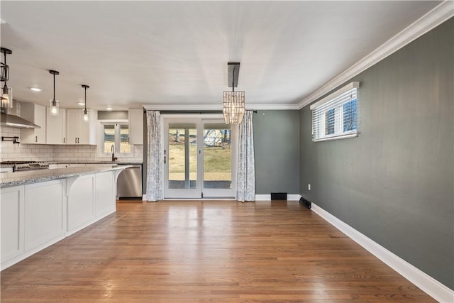 unfurnished dining area with baseboards, ornamental molding, wood finished floors, an inviting chandelier, and a sink