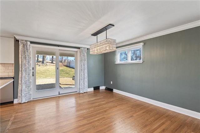 unfurnished dining area with baseboards, crown molding, and wood finished floors