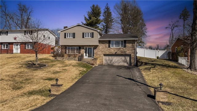 split level home featuring aphalt driveway, an attached garage, fence, a lawn, and a gate