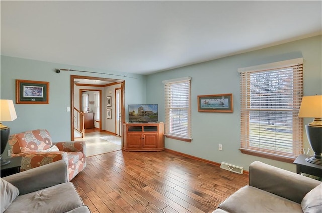 living room featuring hardwood / wood-style flooring, baseboards, stairway, and visible vents