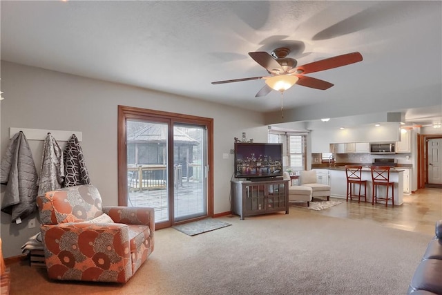 living area with ceiling fan, baseboards, and light colored carpet