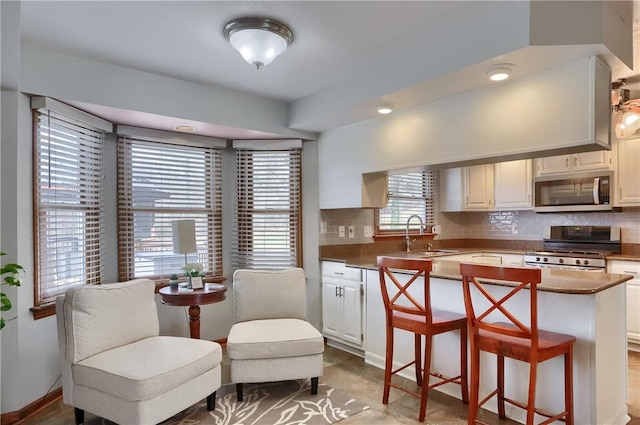 kitchen with a breakfast bar area, stainless steel appliances, backsplash, white cabinets, and a sink