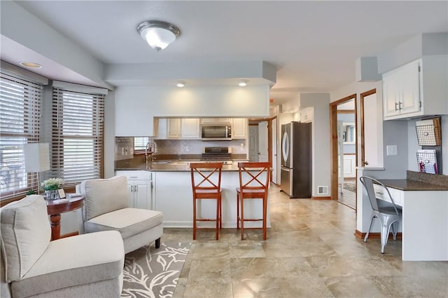 kitchen with a peninsula, appliances with stainless steel finishes, dark countertops, and a sink