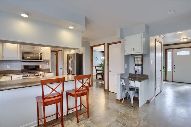 kitchen featuring stainless steel appliances, dark countertops, backsplash, and a kitchen breakfast bar