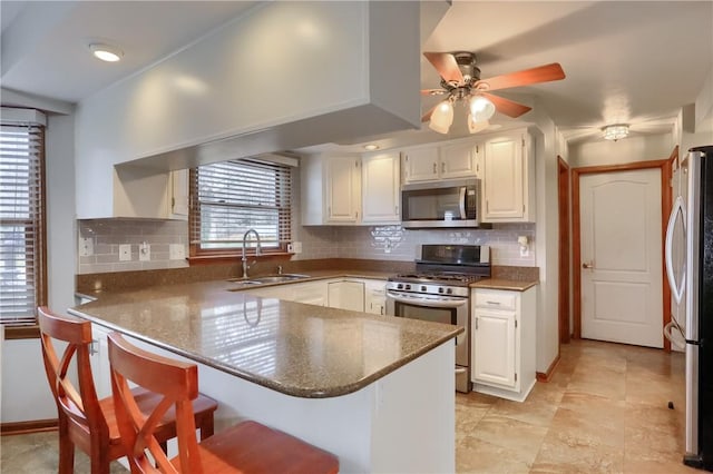 kitchen with a peninsula, white cabinetry, appliances with stainless steel finishes, and a sink