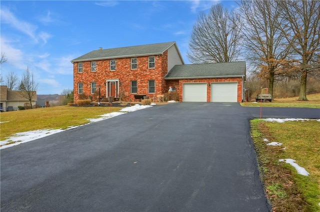 colonial inspired home featuring an attached garage, driveway, a front lawn, and brick siding