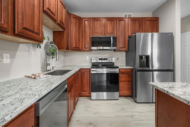 kitchen featuring stainless steel appliances, a sink, visible vents, light stone countertops, and light wood finished floors