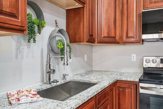 kitchen with light stone countertops, electric range, and a sink