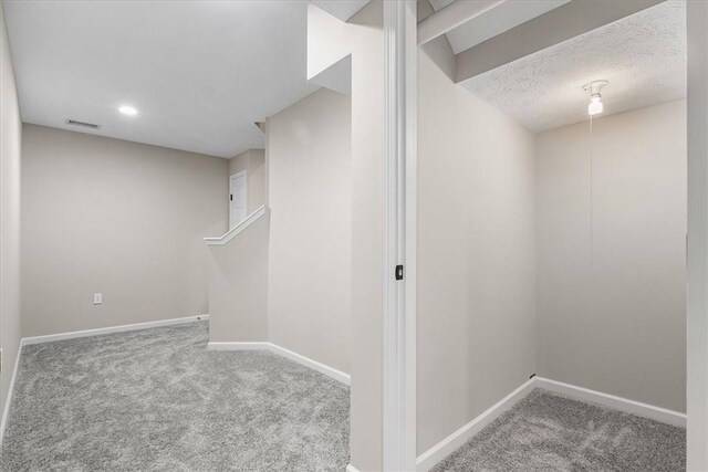 finished basement featuring carpet, visible vents, baseboards, and a textured ceiling