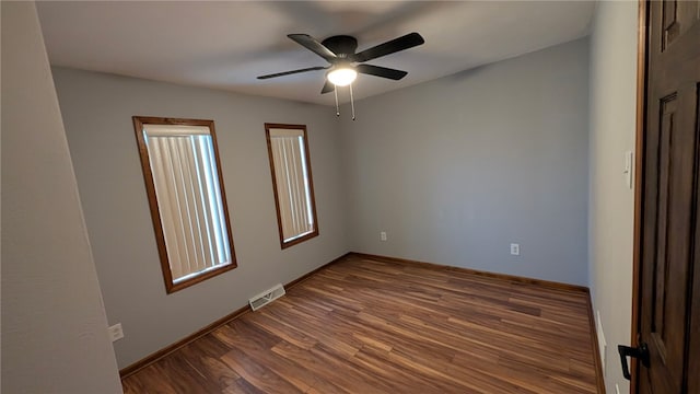 spare room with dark wood-style floors, ceiling fan, visible vents, and baseboards