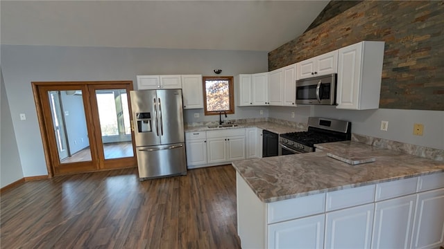 kitchen featuring lofted ceiling, light stone counters, a peninsula, stainless steel appliances, and a sink