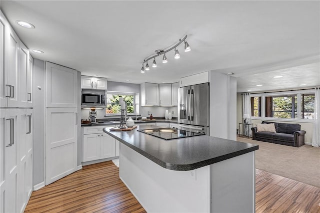 kitchen with dark countertops, appliances with stainless steel finishes, open floor plan, wood finished floors, and a center island