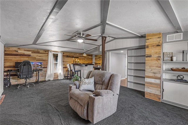 carpeted living area featuring vaulted ceiling with beams, ceiling fan, wooden walls, and visible vents