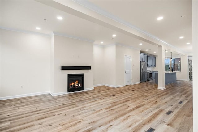 unfurnished living room with recessed lighting, light wood-style flooring, ornamental molding, a lit fireplace, and baseboards