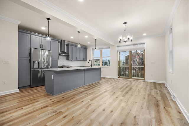 kitchen with stainless steel fridge, wall chimney exhaust hood, gray cabinets, crown molding, and backsplash