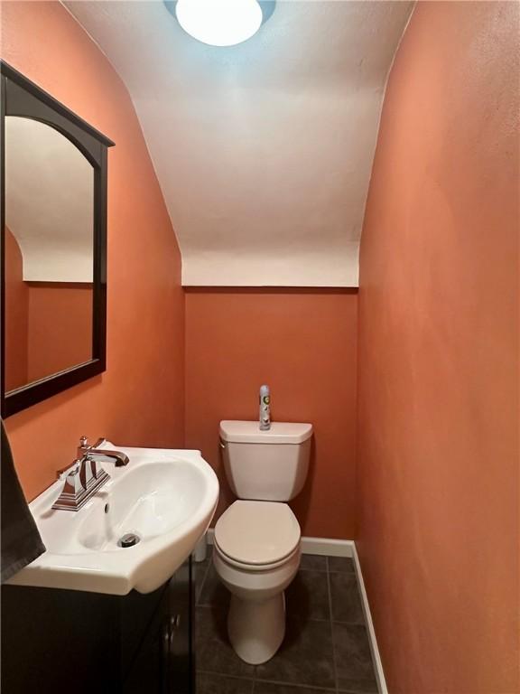 bathroom with baseboards, toilet, lofted ceiling, tile patterned floors, and vanity