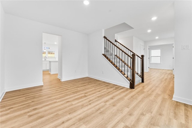 unfurnished living room with light wood-type flooring, baseboards, and stairs