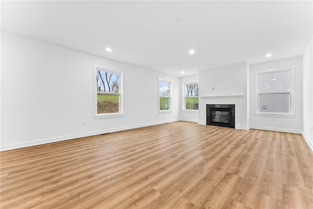 unfurnished living room featuring a glass covered fireplace, baseboards, light wood finished floors, and recessed lighting