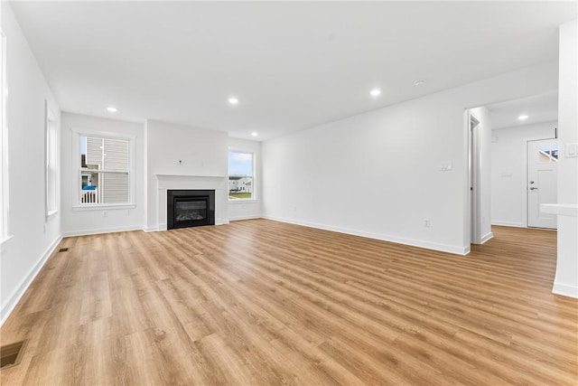 unfurnished living room featuring light wood-type flooring, a glass covered fireplace, and recessed lighting