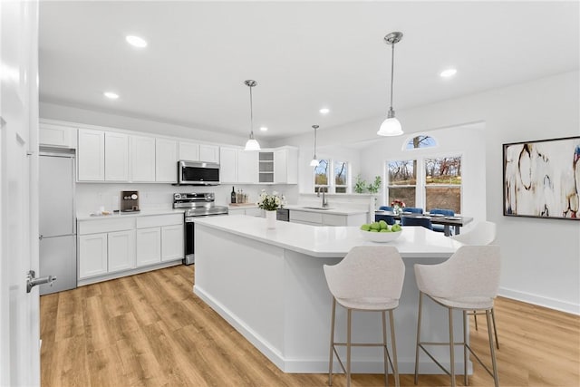 kitchen with stainless steel appliances, a sink, a kitchen island, light wood-style floors, and light countertops