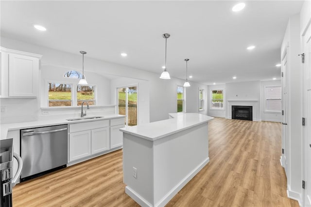 kitchen with stainless steel dishwasher, light wood-style flooring, a sink, and white cabinetry