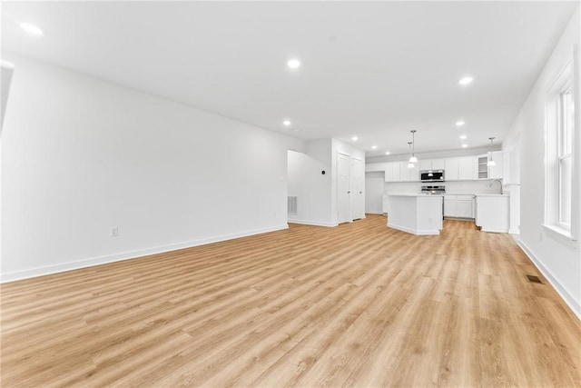 unfurnished living room with light wood-style floors, recessed lighting, a sink, and baseboards