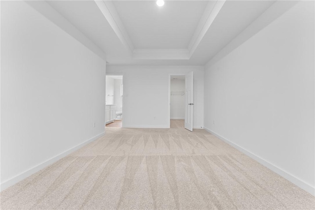 unfurnished bedroom featuring connected bathroom, light carpet, baseboards, a tray ceiling, and a walk in closet