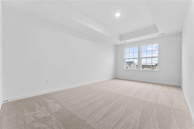 carpeted empty room with a tray ceiling, visible vents, baseboards, and recessed lighting