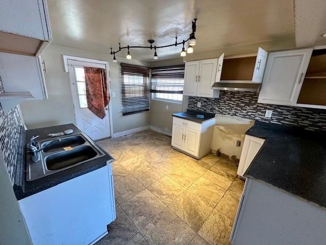 kitchen with tasteful backsplash, baseboards, white cabinets, dark countertops, and a sink