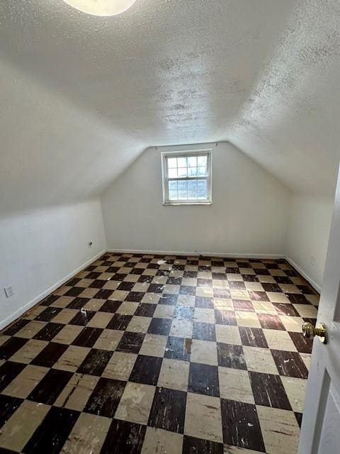 additional living space featuring a textured ceiling, vaulted ceiling, tile patterned floors, and baseboards