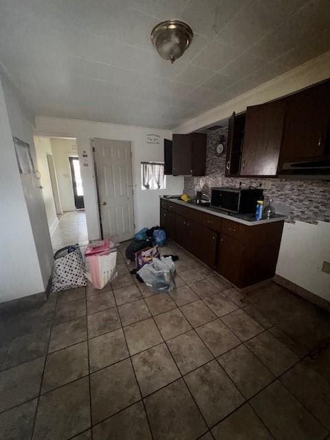 kitchen with dark tile patterned flooring, black microwave, dark brown cabinets, and decorative backsplash