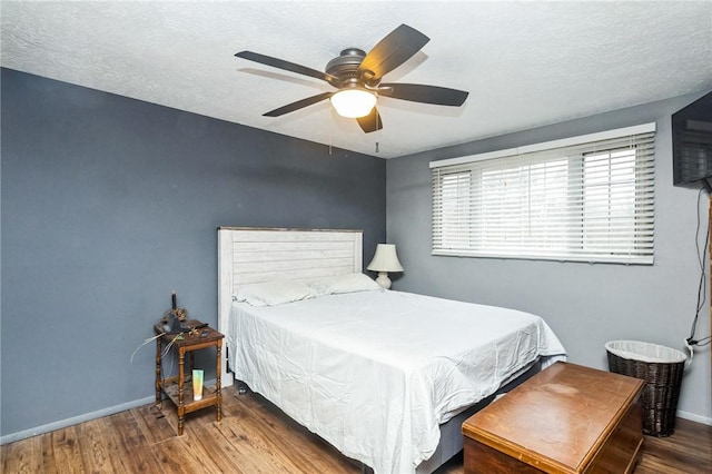 bedroom featuring ceiling fan, a textured ceiling, baseboards, and wood finished floors