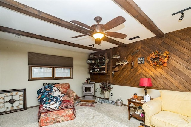 living room with visible vents, ceiling fan, a wood stove, wood walls, and beam ceiling