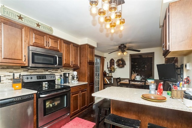 kitchen featuring brown cabinets, appliances with stainless steel finishes, decorative backsplash, and a kitchen breakfast bar