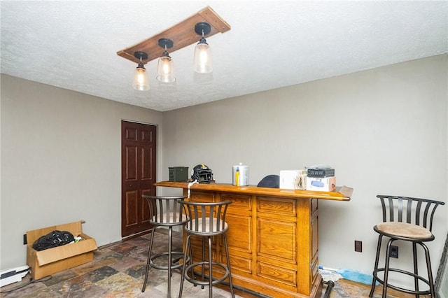 bar featuring a dry bar, stone finish floor, baseboard heating, and a textured ceiling