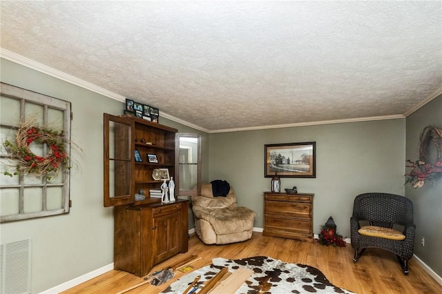 living area with ornamental molding, wood finished floors, visible vents, and baseboards