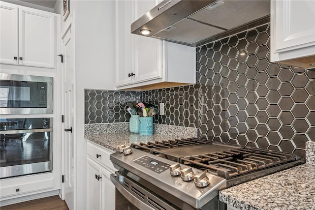 kitchen featuring light stone counters, decorative backsplash, appliances with stainless steel finishes, white cabinetry, and under cabinet range hood