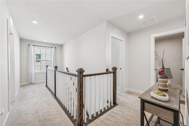 hall featuring light carpet, visible vents, an upstairs landing, and baseboards