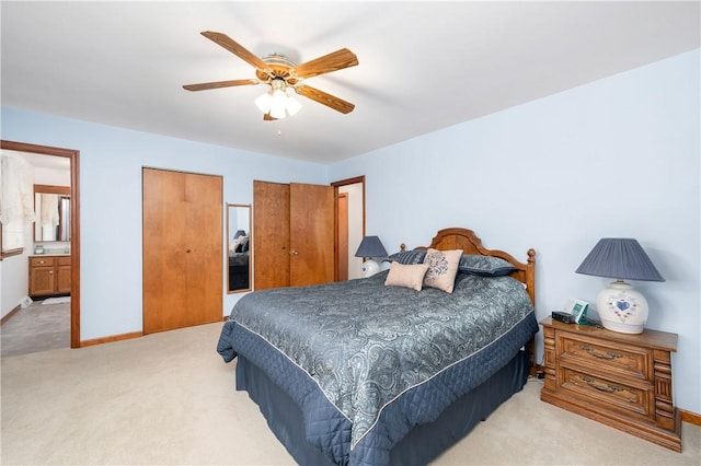 bedroom featuring ensuite bathroom, light colored carpet, a ceiling fan, baseboards, and two closets