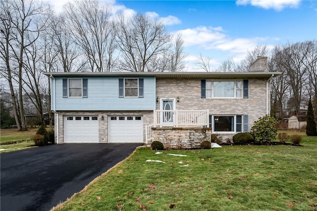 bi-level home featuring a garage, a chimney, aphalt driveway, a front lawn, and brick siding