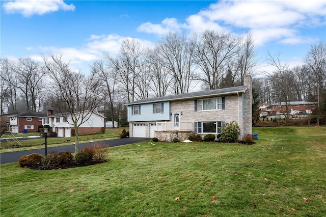 bi-level home featuring driveway, stone siding, a chimney, an attached garage, and a front yard